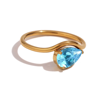 gold ring with a blue crystal placed within the ring placed on a white background
