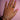 A hand with pink manicured nails on a pink background, adorned with multiple gold rings and two glittering bracelets, exuding elegance and style.