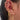 A close-up of a woman's ear adorned with an eclectic mix of gold earrings, including sparkly ear cuffs, chain drop hoops, star and crystal stud motifs, and a dangling planet charm. The ear features multiple piercings and is styled in a bold, curated stack that blends celestial and classic designs.