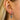 Close-up of a woman's ear wearing a sparkling silver hoop earring with a blue heart-shaped gemstone charm surrounded by clear crystals – stylish and elegant accessory.