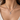 A close-up of a model's neck and chest wearing a silver chain necklace with a letter 'A' initial pendant, a small ring charm, and a tiny lavender crystal accent.