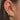 Close-up of an ear with multiple opal old earrings against a neutral background
