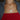 Woman's neck adorned with layered gold necklaces featuring a clover and round pendant, over a red ribbed top and gray zip-up sweater. Elegant and stylish.