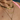 Close-up of a layered gold necklace look worn by a person in a pink top, featuring a bold heart charm choker, braided gold chain with pearls, a gold name necklace reading "Natalia", and a floral pendant with pink and white gemstones.
