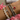 Stack of silver charm bracelets with pearls, crystal accents, and a red enamel heart, styled on wrist with Binky Belle satin pouches in the background.