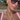 Woman wearing sunglasses and a pink top with layered necklaces outdoors.