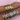 Two wrists adorned with an array of gold and silver bracelets, featuring heart motifs and Roman numerals, displayed on a light pink fabric.