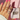 A hand with pink nails displays multiple gold and silver rings with diamond accents. A "Binky Belle" jewelry box is partially visible on a pink background.