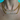 Close-up of a person wearing two thick gold chain necklaces with diamond-encrusted name pendants. The upper pendant reads “NATALIA” and the lower one says “BINKYBELLE.” The person is dressed in a white swimsuit with red scalloped trim, and a turquoise pool is visible in the background.