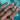 A hand with glossy pink nails elegantly showcases three stacked tri-band rings in front of a pool. Each ring intertwines gold, silver, and pavé-set bands, creating a bold, luxury statement with a playful, summer-ready vibe.