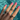 A hand with glossy pink nails displays three intertwined tri-tone rings—each blending gold, silver, and pavé-set bands—against the sparkling blue water of a pool.