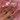 A hand with pink manicured nails showcases three tri-tone intertwined rings—each combining gold, silver, and pavé-set bands—on a soft pink satin background, with a lilac Binky Belle jewellery box in the backdrop.