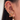 Close-up of a woman's ear adorned with multiple gold earrings in various styles, including hoops with pavé crystals, a pink enamel bow dangle, a heart-shaped crystal drop, and several star and cluster studs. The look is bold, elegant, and highly curated.