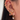 Close-up of a woman's ear adorned with multiple gold earrings in various styles, including hoops with pavé crystals, a pink enamel bow dangle, a heart-shaped crystal drop, and several star and cluster studs. The look is bold, elegant, and highly curated.