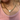Person wearing a gold chain necklace with a heart pendant on a pink top.