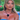 Blonde woman wearing a strapless blue dress and statement Dior chain choker necklace with sparkly teardrop earrings, seated during a reality TV show moment.