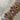Close-up of a forearm adorned with a vibrant stack of gold bangles featuring crystal accents, enamel hearts, Roman numerals, clover motifs, and unique charm details, all set against a neutral tiled background.