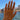A hand with manicured nails wearing a delicate gold chain hand bracelet and several rings, set against a sunny beach background with blue water and buildings.