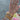 A close-up of a hand wearing multiple gold rings, a delicate gold chain bracelet, and several stacked bangles, including one with the name 'BELLE' in white letters. The hand has light pink manicured nails, and a patterned clutch is partially visible in the background.