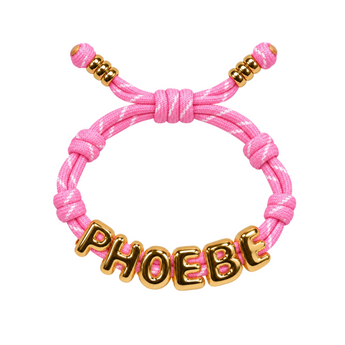 A pink braided cord bracelet with a sliding knot closure, gold spacer beads, and a gold metal nameplate spelling 'PHOEBE' in raised letters, shown on a plain white background.