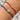 Two delicate cord bracelets on a person's wrist, one in red and one in blue, both featuring a small gold-tone floral charm set with clear stones and gold spacer beads.