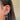 Close-up of an ear adorned with multiple silver earrings, including studs, hoops, and dangling chains featuring crystals, against brown hair.