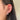 Close-up of an ear adorned with multiple piercings, featuring star-shaped and crystal-studded earrings. The hair is dark and straight, creating a stylish tone.