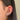 Close-up of an ear adorned with multiple silver earrings, including hoops and studs, set against long, dark hair. The image conveys a stylish and edgy tone.