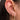 A close-up of an ear adorned with three gold earrings. The first is a small dangling stud with a floral diamond-shaped design. The second is a simple, chunky gold huggie hoop. The third is a larger hoop encrusted with tiny clear stones, featuring a dangling starburst charm also set with stones. The jewellery is gold-toned, and the wearer’s dark hair is tucked behind the ear, creating a clean and elegant look.