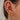 A close-up of a woman's ear adorned with multiple gold earrings, including hoops, studs, and cuffs. Designs feature sparkly crystals, stars, chains, and celestial motifs. The ear is styled with a curated mix of dainty and statement pieces, creating a layered, glamorous look.