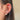 Close-up of an ear adorned with multiple earrings: a gold and crystal leaf design in the cartilage, small studs in the lobe, and constellation shapes.