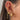 Close-up of an ear adorned with multiple gold and pink-themed earrings. The upper cartilage features a pink heart stud paired with a dangling crescent moon charm, a pink butterfly-shaped stud, and sparkly cuff hoops. The mid-section displays a gold cuff with pavé stones, while the lobe showcases a layered look with several hoops. These include a chunky gold hoop with star engravings, a gem-studded hoop with a dangling pink heart charm, and a longer chain earring with small stars.