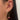 Close-up of an ear with three earrings: a gem-studded hoop, a gold chain with a pink heart pendant, and a smaller star-shaped stud with a gem. Elegant and stylish.