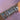 A forearm adorned with multiple silver and gold bracelets featuring heart shapes, Roman numerals, and various gem patterns, set against a pink fabric background.