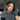 Woman with sleek black updo wearing bold red lipstick, pearl statement earrings and black fitted t-shirt, posing in natural sunlight inside modern luxury living room.