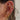 A gold celestial ear stack with dreamy detailing. The look features an opal crescent moon and star earring, pave huggies, and a dangling double star charm. Cluster studs and engraved hoops add dimension, while a compass-style charm hangs delicately from the upper lobe. A chic, astrology-inspired vibe.