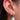Close-up of an ear adorned with three gold earrings. Two feature small diamonds, and one large hoop holds a hanging white pearl. Elegant and luxurious.