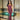 Stylish woman in a strapless burgundy mesh corset dress with black detailing, wearing pointed heels and a cross necklace, posing confidently by an indoor pool