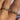 Close-up of gold-plated crystal rings worn on fingers with red nail polish, featuring floral and baguette-cut designs under natural sunlight
