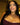 Model wearing crystal cross pendant necklace with gold chain, styled with plum strapless top and glam makeup