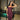 Woman wearing deep burgundy corset maxi dress and gold cross necklace, posing indoors by a glass door and lit-up plunge pool