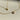 Two delicate gold necklaces displayed on a cream surface, one featuring a small heart pendant with a single clear stone, and the other showcasing a floral clover pendant encrusted with sparkling crystals.