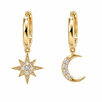 A pair of gold huggie hoop earrings, one featuring a dangling starburst charm set with clear crystals and the other a crescent moon charm also set with clear crystals, shown on a plain white background.