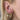 Close-up of an ear with three elegant gold hoop earrings. Two have dangling heart and key charms, and the third features a blue floral design. Hair is light blond.