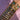 A forearm adorned with a stack of 16 gold bangles, featuring various designs like hearts, stars, and gems, set against a soft pink fabric background.