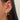 Close-up of an ear wearing two earrings: a gold hoop with embedded gems and a dangling chandelier design with star shapes, conveying elegance and style.