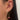 Close-up of an ear adorned with three earrings: a gem-studded hoop, a dangling heart-shaped pendant with a pink gem, and a small star-shaped stud.