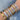 A wrist adorned with multiple shiny bracelets featuring gold and silver tones, embellished with star, heart, sun motifs, and sparkling crystals, set against a wet metallic surface.