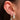 Close-up of a gold ear stack featuring a crystal flower stud, a drop hoop with a clover charm, and a bold pavé teardrop statement earring on a woman’s ear.