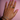 A hand with pink nail polish is adorned with multiple rings and bracelets in gold and silver tones, featuring heart motifs, rhinestones, and elegant curves, resting against a pastel pink background.